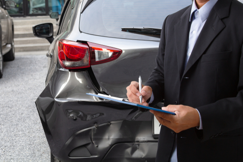 examining car accident damage while writing on clipboard