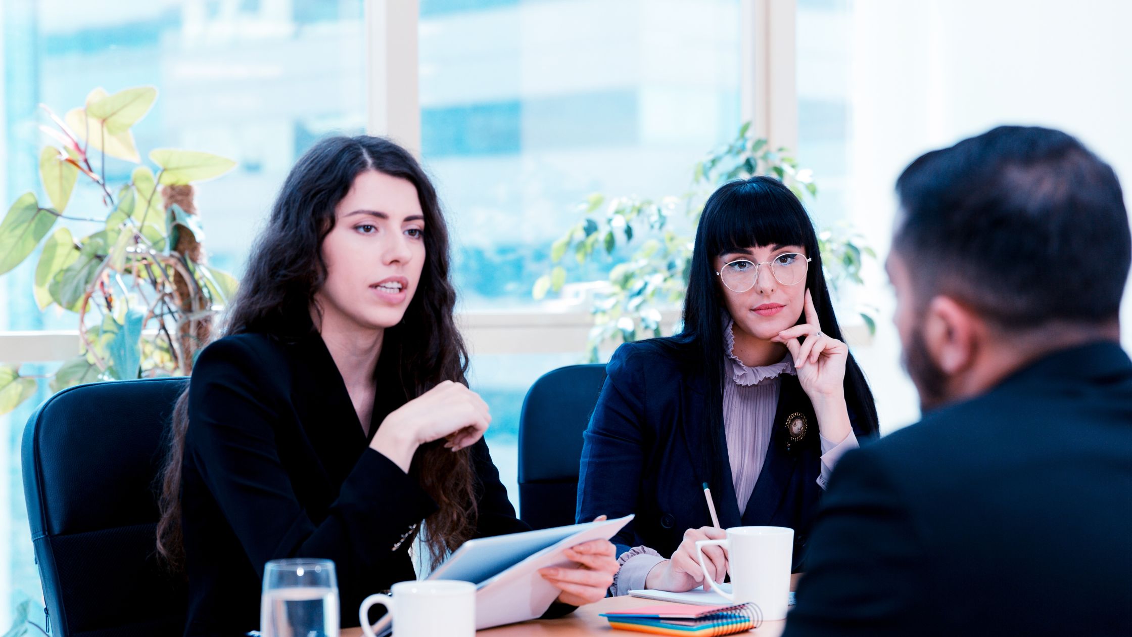 wo professional women attentively listening to a man during a discussion, reflecting a strategic meeting on common defenses used by insurance companies in personal injury cases.