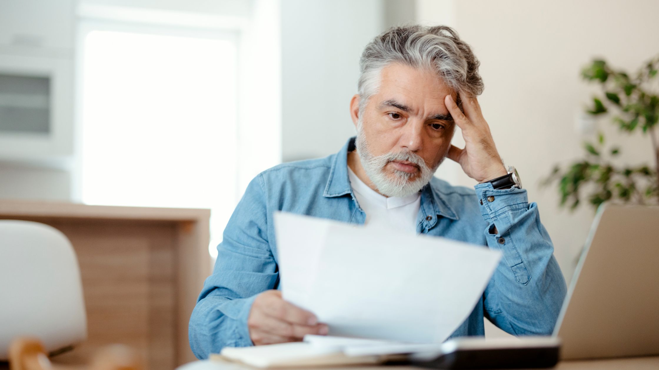Concerned senior man reviewing documents, facing financial strain with medical bills exceeding his car accident settlement.